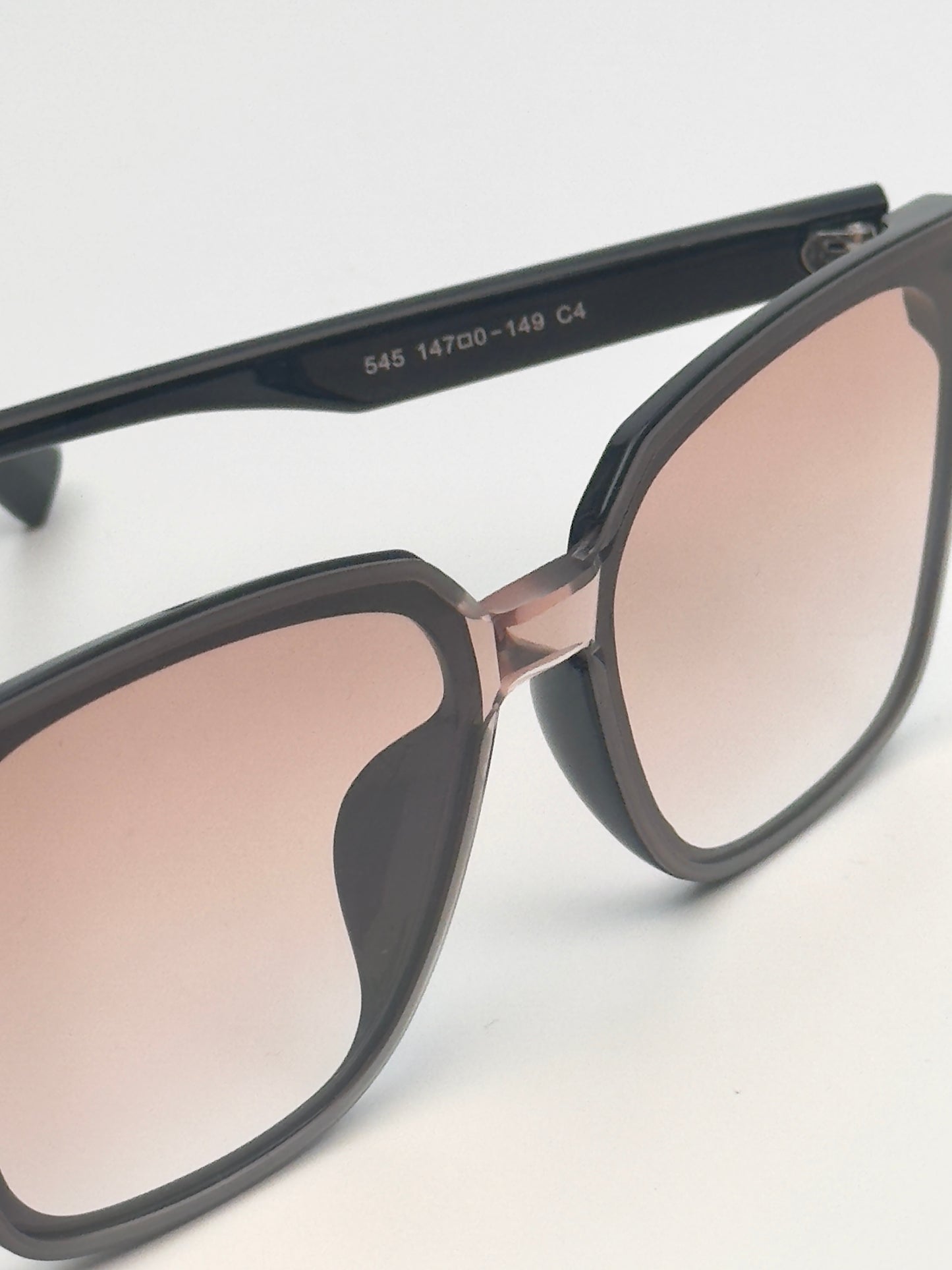 Sunglasses with black frame and pink gradient lenses on a light gray background